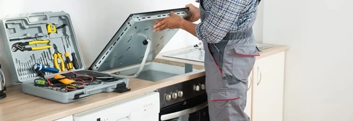 Cooktop repair technician lifting a built-in stovetop for service in San Francisco, CA