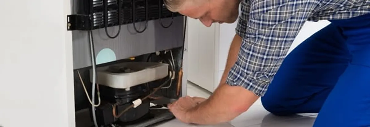 Refrigerator repair technician servicing the compressor and condenser area in San Francisco, CA